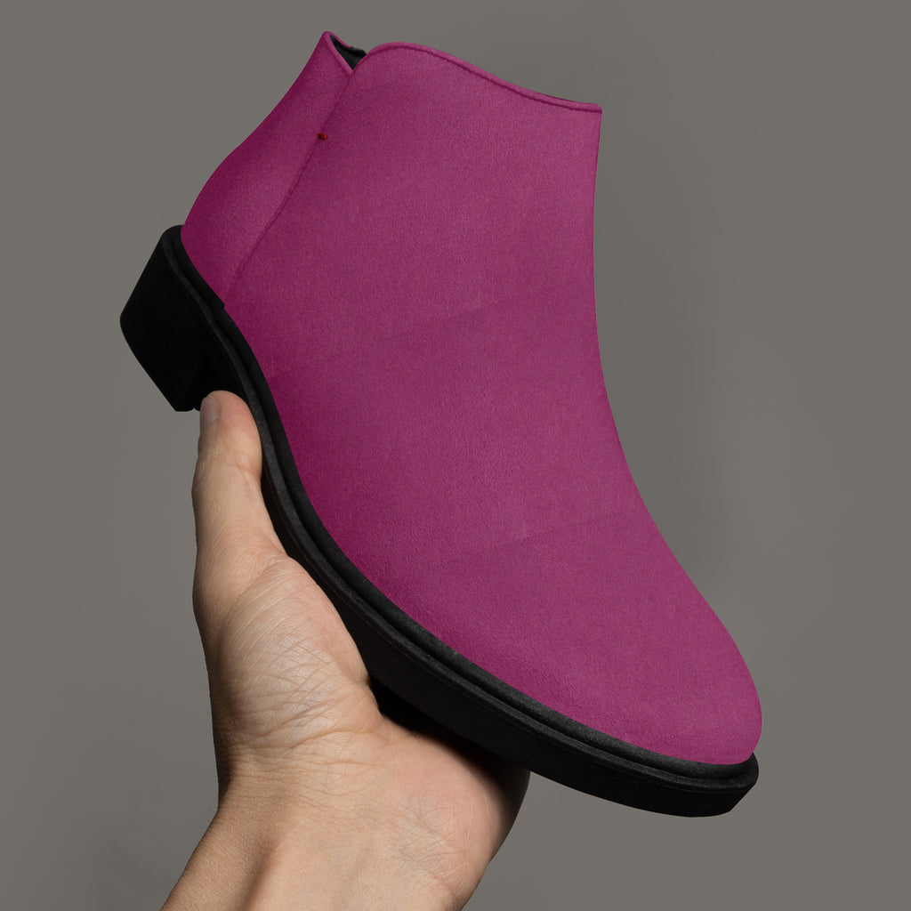 Magenta suede ankle boot with scalloped top edge and chunky black heel held in hand against gray background.