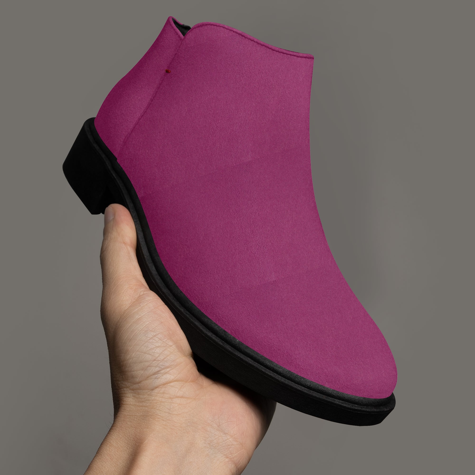 Magenta suede ankle boot with scalloped top edge and chunky black heel held in hand against gray background.