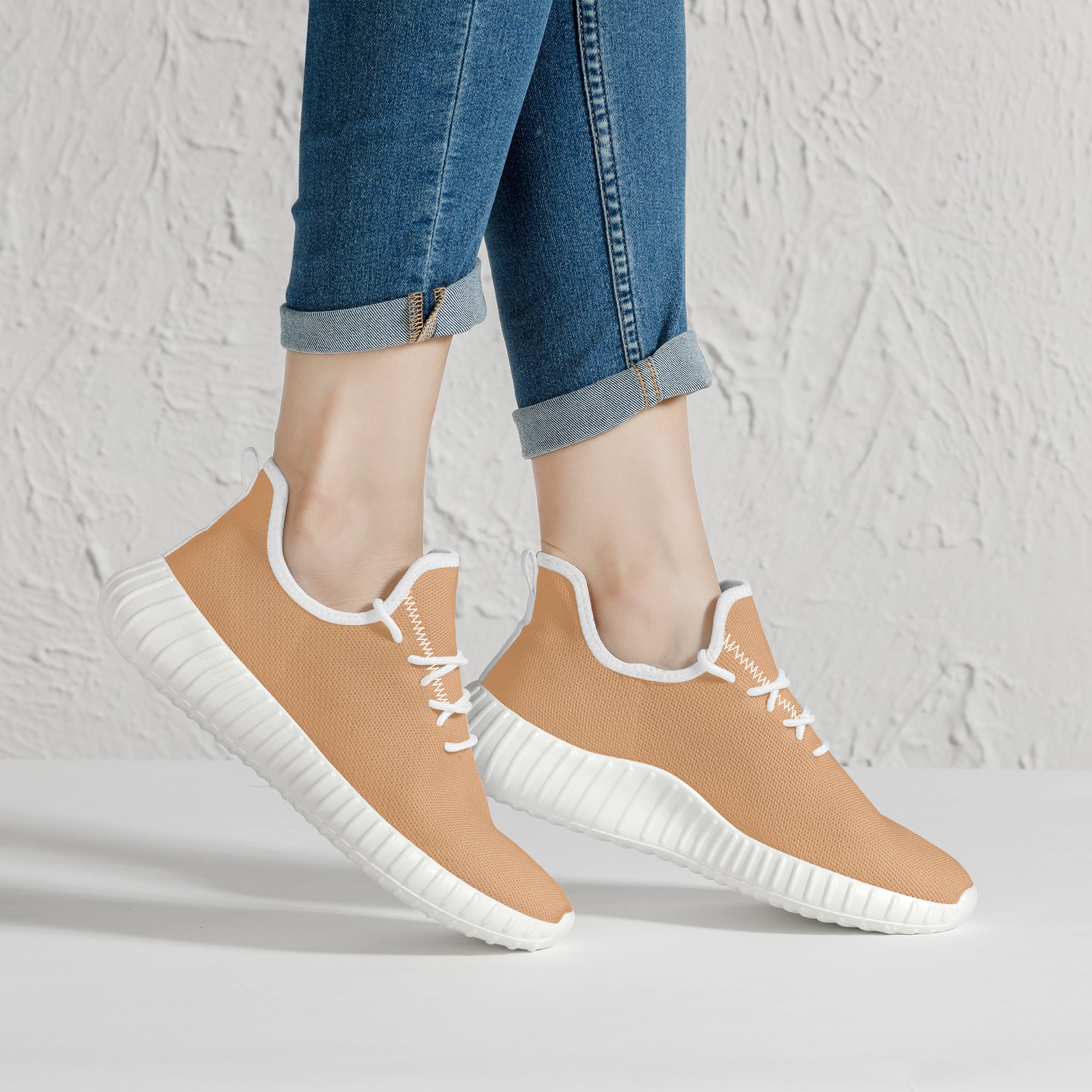 Beige low-top knit sneakers with white soles and laces, worn with cuffed blue jeans.