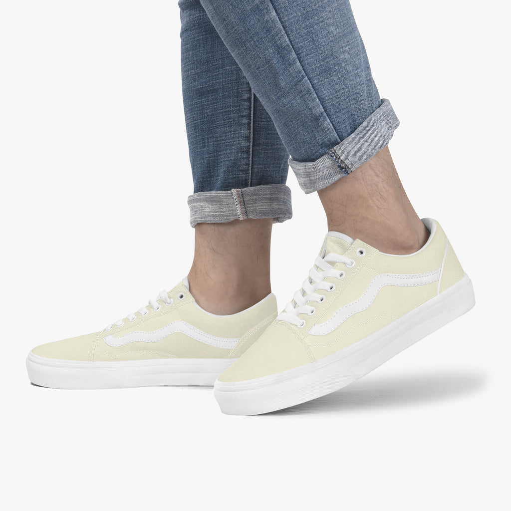 Pale yellow low-top canvas sneakers with white laces and white rubber soles worn with cuffed jeans.