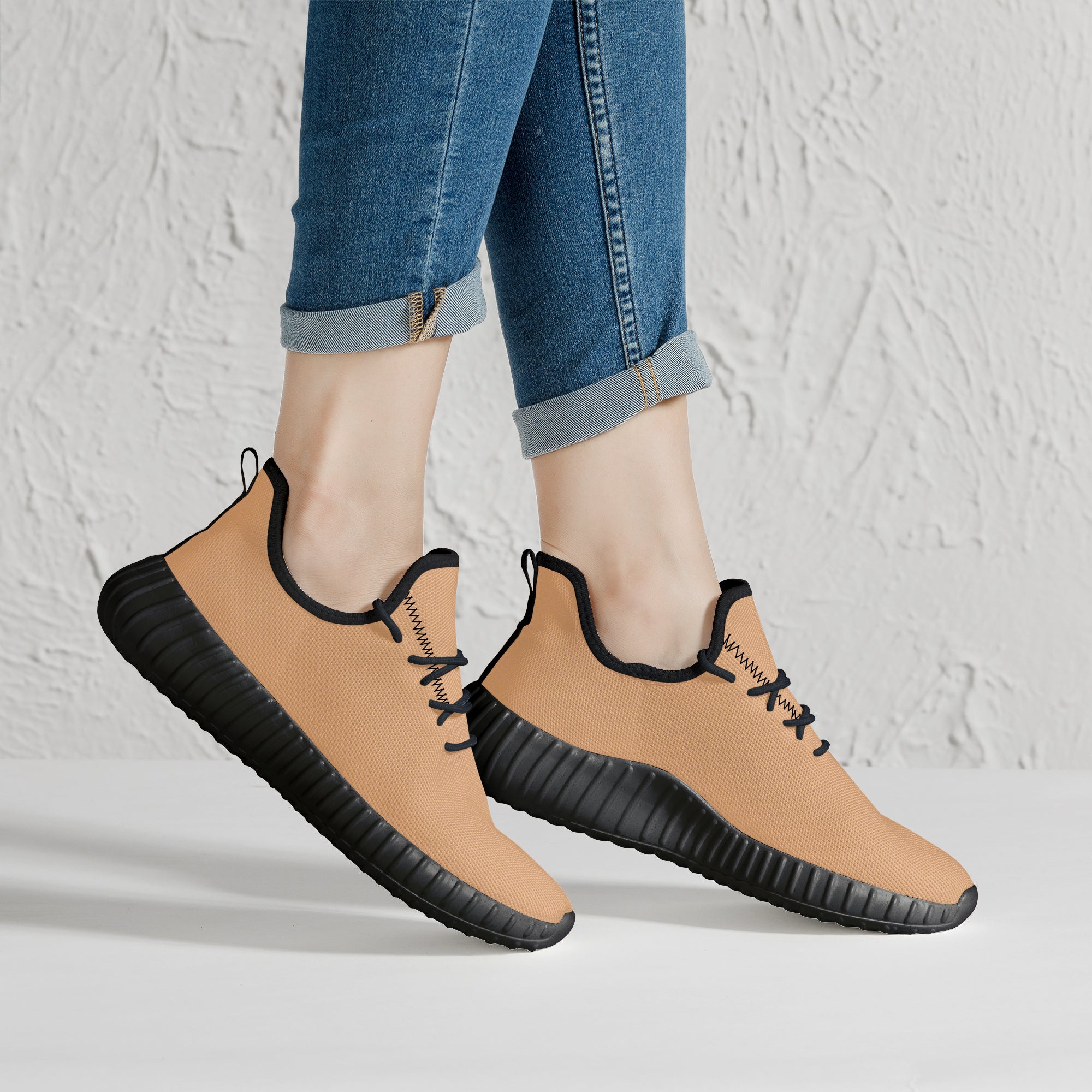 Beige mesh knit low-top sneakers with black soles and laces worn with rolled-up jeans.