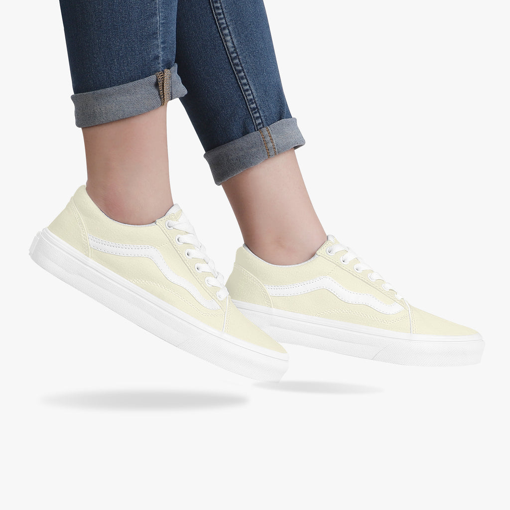 Pale yellow low-top canvas sneakers with white laces and thick white rubber soles worn with cuffed dark jeans.