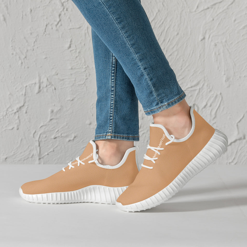 Beige low-top mesh knit sneakers with white laces and flexible white sole worn with blue skinny jeans.